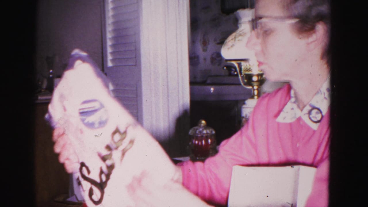Woman in pink sweater with white collar examining a branded package at Christmas, circa 1962, Hagerstown Maryland; brass candlestick and interior shelving visible.