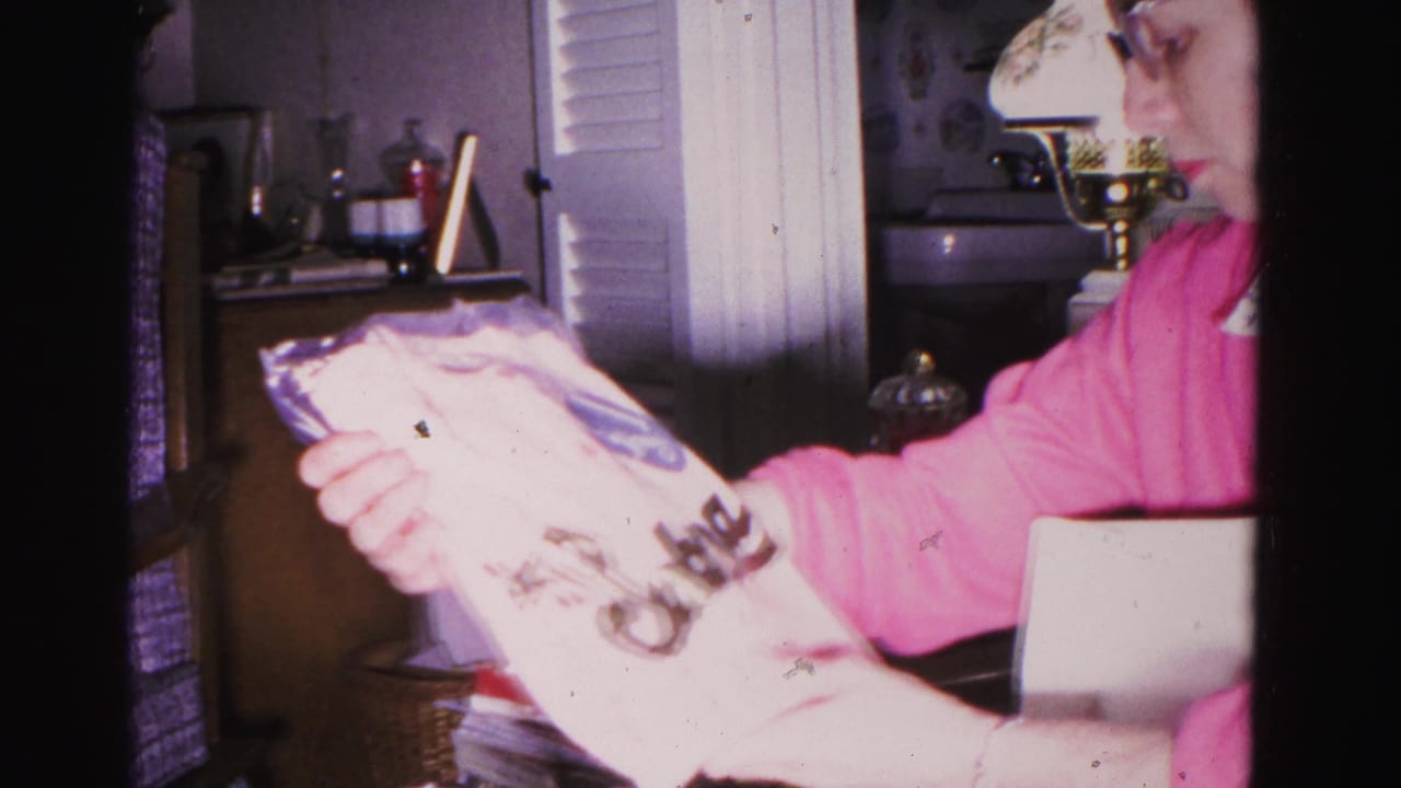 Woman in pink sweater inspecting printed gift packaging, circa 1962, Hagerstown Maryland; window with blinds and shelf furnishings visible in background.