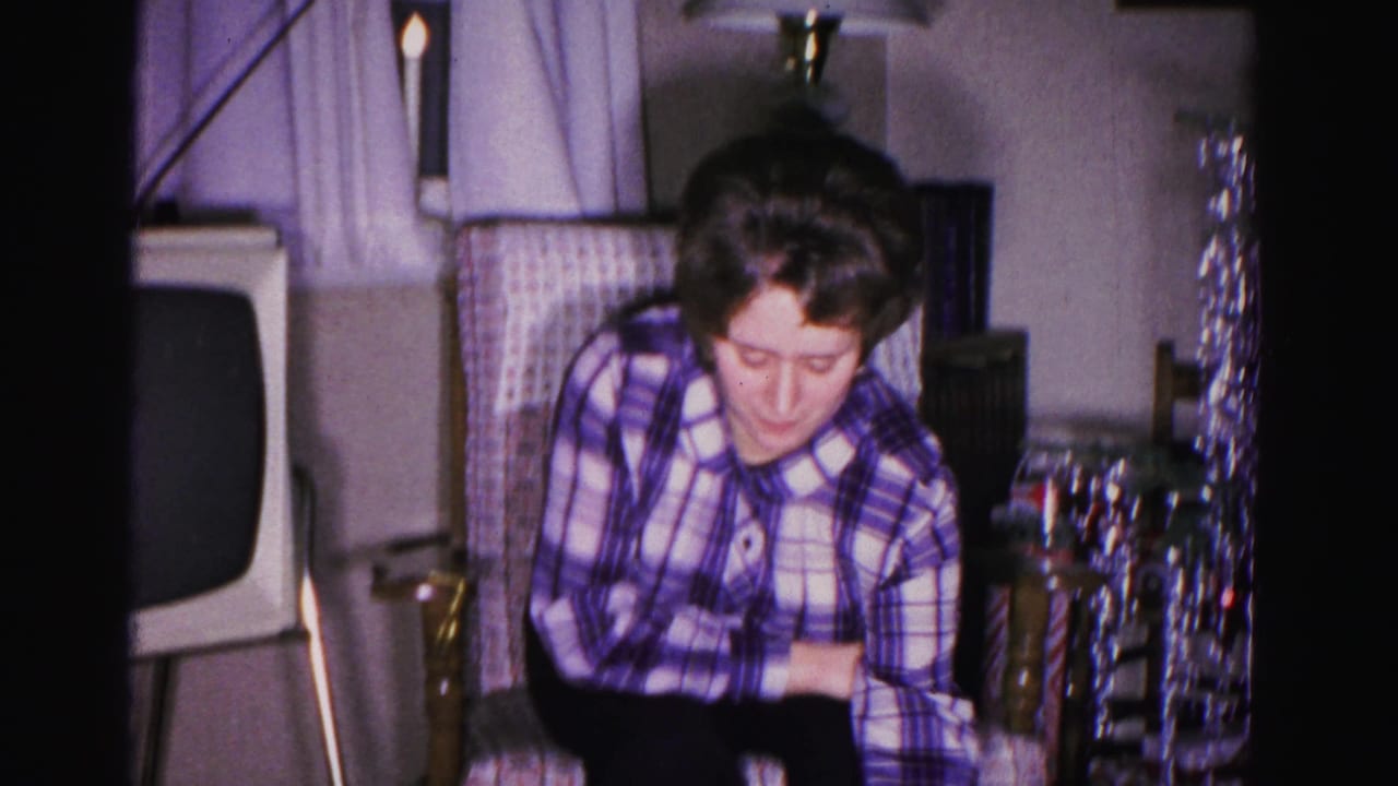 Woman in plaid blouse examines blue gift box; vintage television and silver tinsel visible in background; 8mm home movie, Hagerstown, Maryland, 1962.