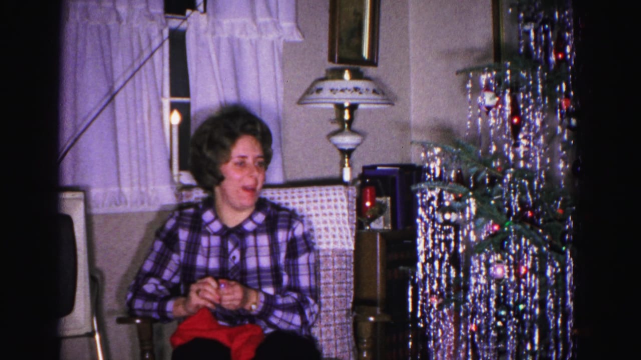 Woman in purple plaid shirt smiles beside a dense silver tinsel Christmas tree with colored ornaments and a tall decorative table lamp, Hagerstown MD, 1962.