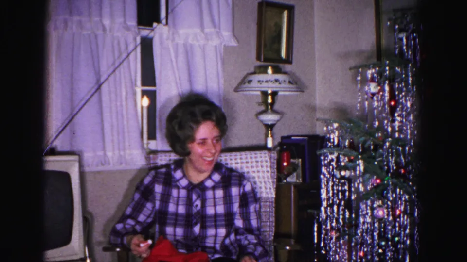 Woman in purple plaid shirt laughs openly beside a silver tinsel Christmas tree with colored ornaments and a tall decorative lamp, Hagerstown MD, 1962.