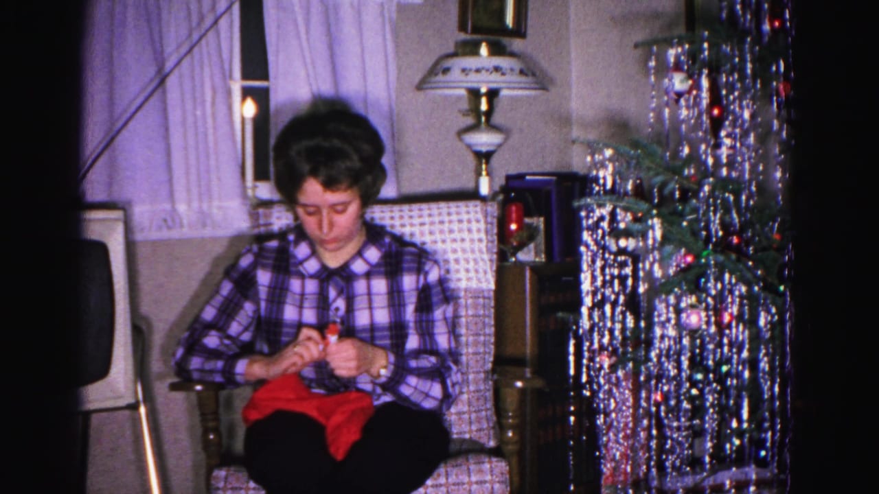 Woman knitting red yarn in an armchair, silver cascade tinsel tree with colored ornaments in background; Hagerstown, Maryland home movie, ca. 1962.