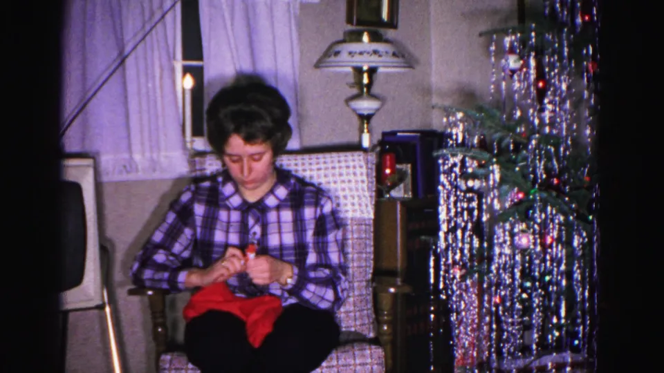 Woman knitting red yarn in an armchair, silver cascade tinsel tree with colored ornaments in background; Hagerstown, Maryland home movie, ca. 1962.