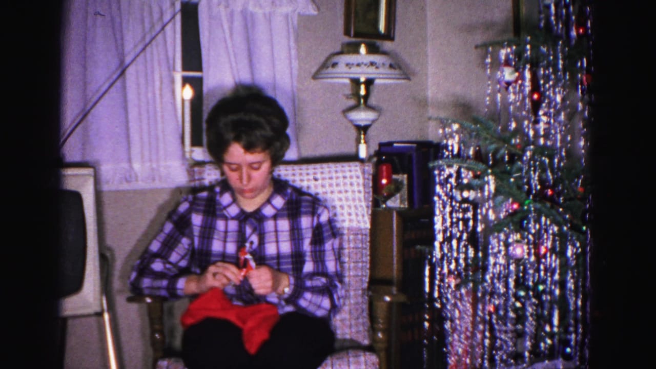 Woman knitting red garment in armchair, silver tinsel tree with ornaments to right, table lamp upper right; Hagerstown, Maryland home movie, ca. 1962.