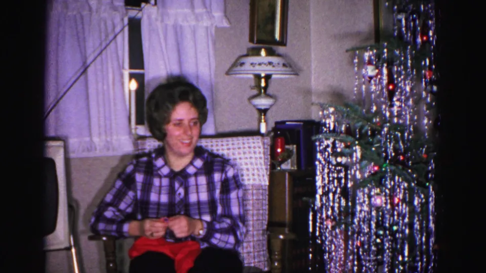 Woman knitting red garment in armchair, silver tinsel strands and table lamp in background; Hagerstown, Maryland home movie, ca. 1962.