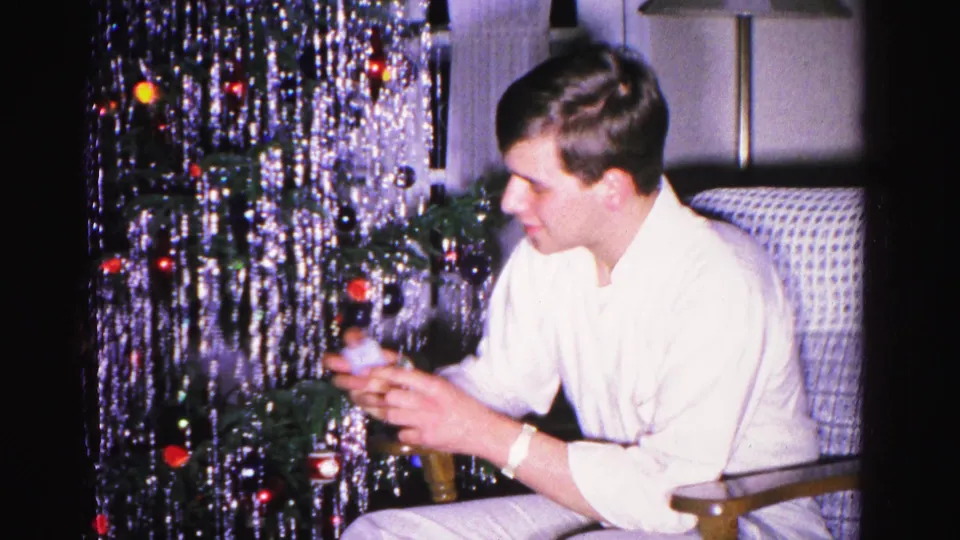 Young man attending to a densely tinseled Christmas tree adorned with colored ornaments in an early-1960s living room, Hagerstown, Maryland, circa 1962.