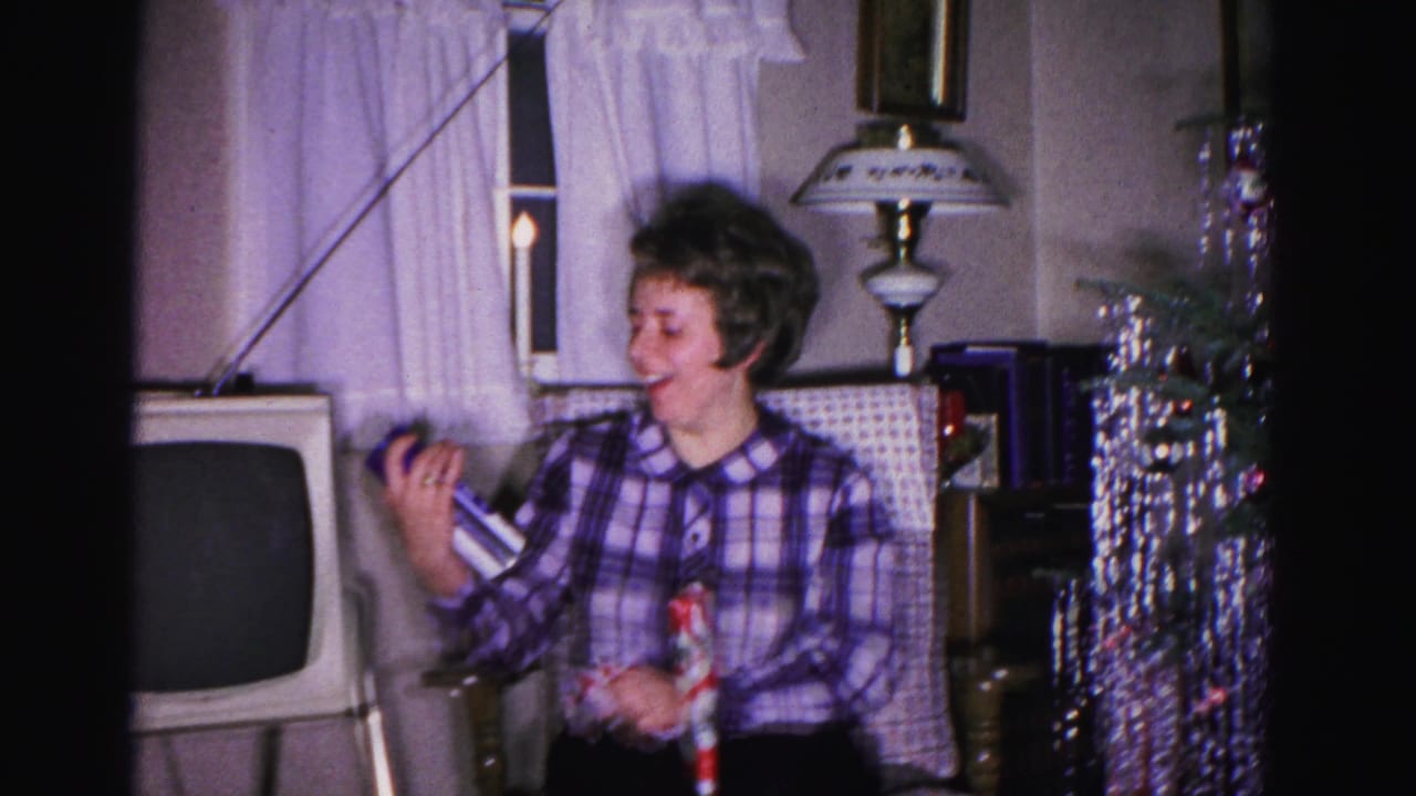 Young woman in plaid blouse laughs during Christmas gift opening; a vintage boxy television and silver metallic tinsel tree are visible in this Hagerstown, Maryland living room, ca. 1962.