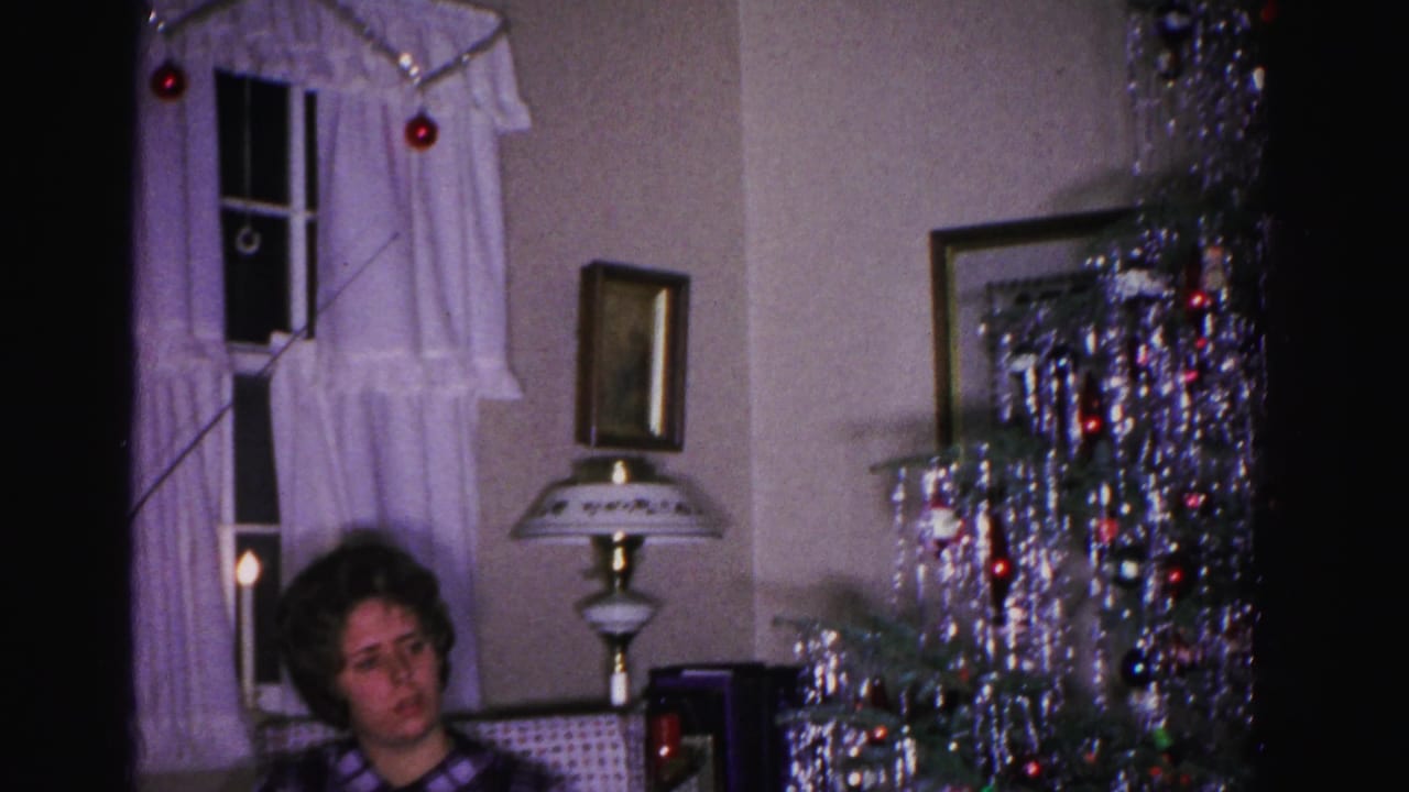 Woman in purple plaid shirt seated in a 1962 Hagerstown, Maryland home interior; silver tinsel Christmas tree, ornate lamp, and curtained window with red ornamental balls behind her.
