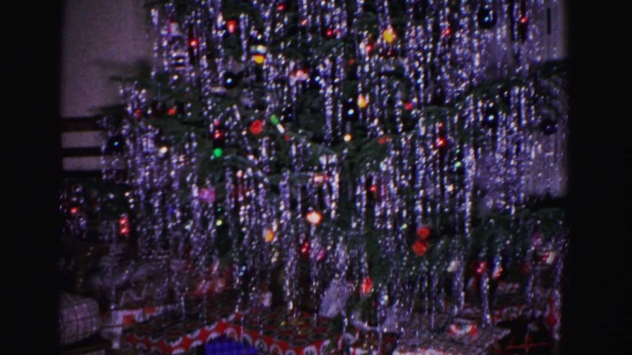 Close-up of a silver-tinsel Christmas tree with multicolored ball ornaments, shot on 8mm in a 1962 American home interior.