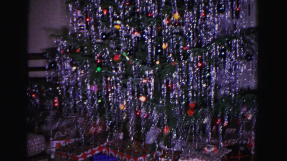 Close-up of a silver-tinsel Christmas tree with multicolored ball ornaments, shot on 8mm in a 1962 American home interior.