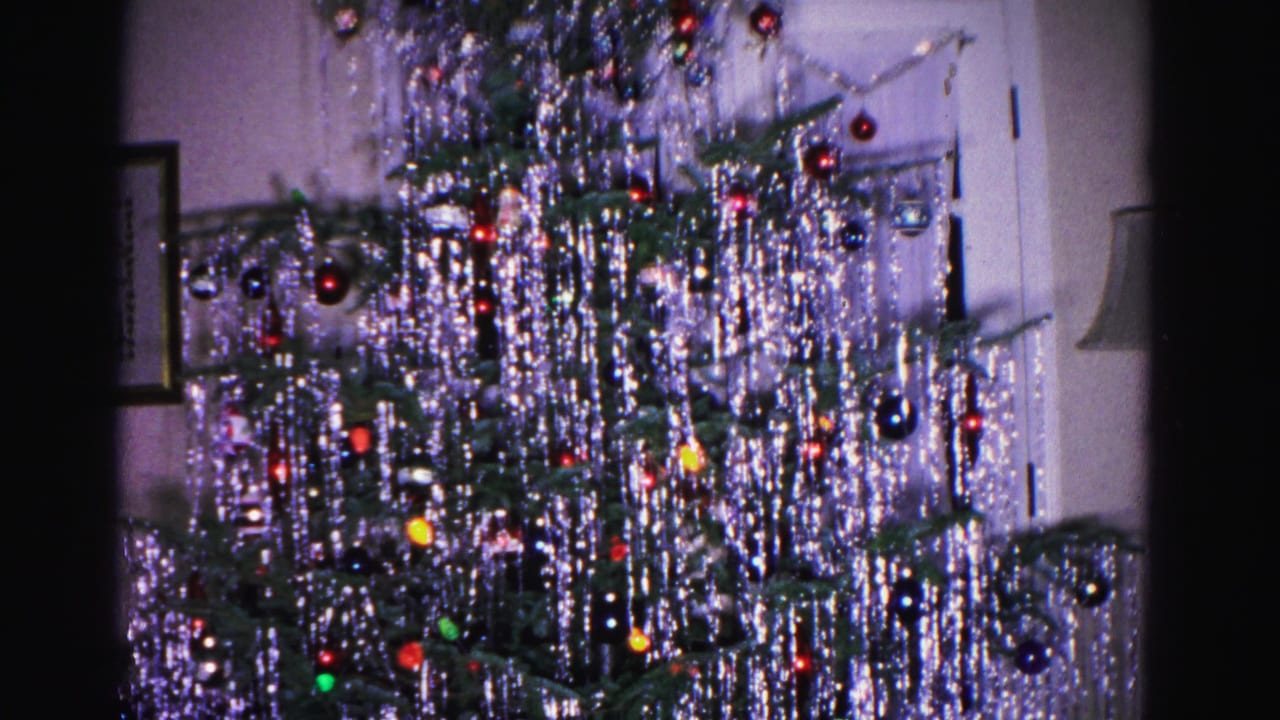 Upper portion of a Christmas tree densely covered in silver icicle tinsel and round glass ornaments, from a 1962 8mm home movie shot in Hagerstown, Maryland.