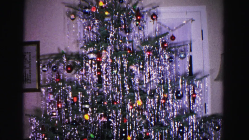 Pan across a tinsel-draped Christmas tree revealing a white interior door and framed wall artwork, from a 1962 home movie in Hagerstown, Maryland.