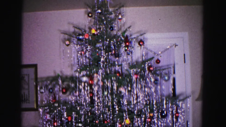 Lower section of a densely tinsel-draped Christmas tree with visible room floor and framed artwork on the wall, from a 1962 8mm home movie in Hagerstown, Maryland.