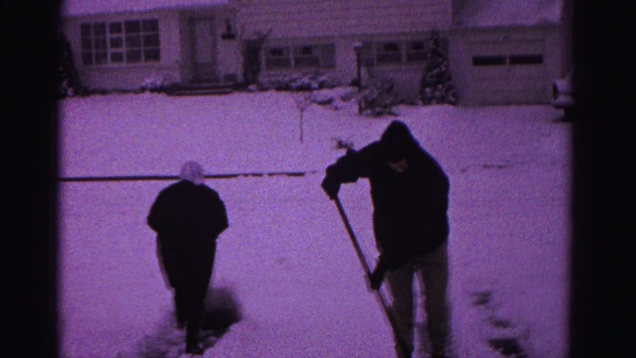 Two individuals clearing snow from a suburban driveway on 8mm film, likely Hagerstown, Maryland, circa 1962; shorter figure appears to wear a light-colored head covering.