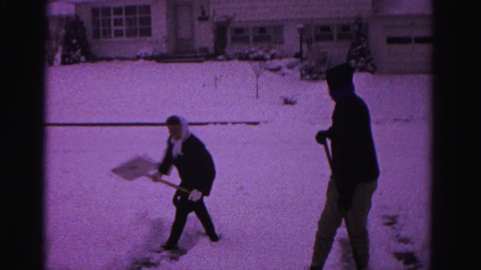 Two household members continue clearing a snow-covered driveway in this final 8mm frame, consistent with Hagerstown, Maryland, circa 1962.