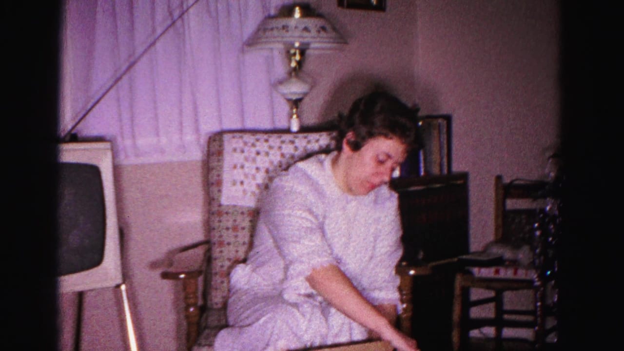 Young woman unwrapping a Christmas present in a 1962 domestic interior in Hagerstown, Maryland; early-sixties television set and ornate mid-century lamp in background.