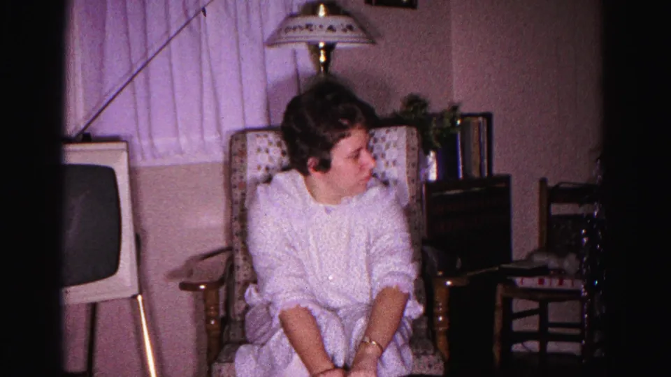 Woman in white robe smiling at RCA Victor gift box during a birthday celebration; 8mm home movie, 1962, Hagerstown, Maryland.