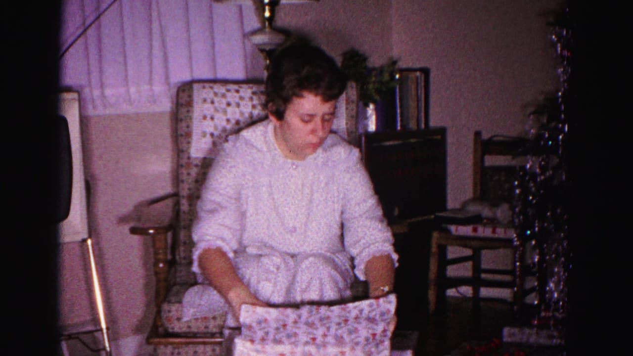 Young woman in white housecoat unwrapping a Christmas gift in a domestic living room, Hagerstown Maryland, circa 1962, 8mm home movie.