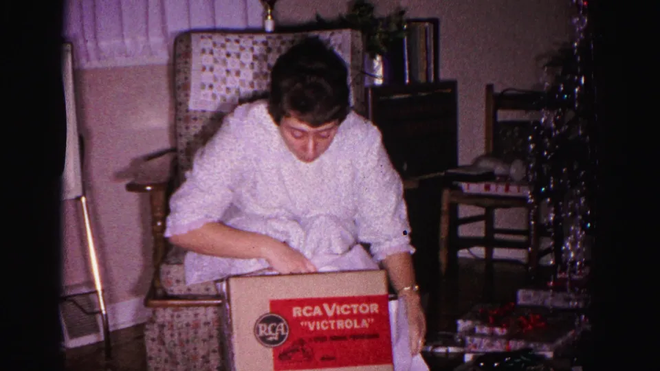 Woman examining the RCA Victor Victrola gift box, Christmas scene in domestic living room, Hagerstown Maryland, circa 1962, 8mm home movie.