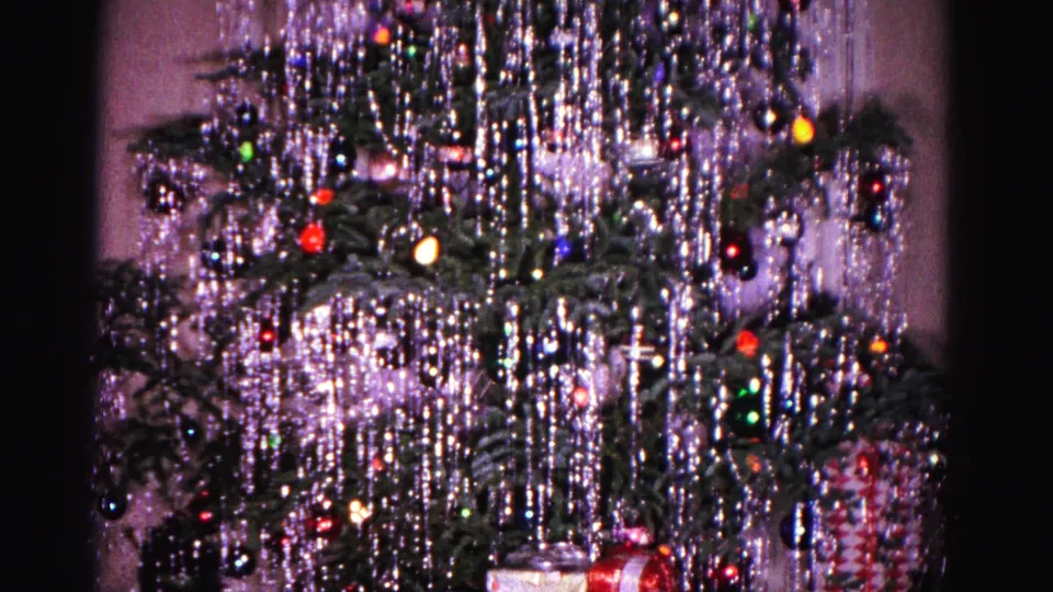 1962 Hagerstown home-movie frame showing a Christmas tree covered in silver tinsel, colored bulbs, ornaments, and wrapped gifts stacked below.