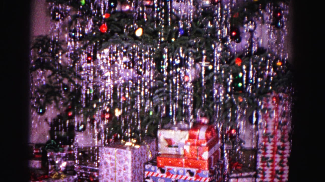 Christmas tree with shiny tinsel and several wrapped gift boxes piled under the branches.