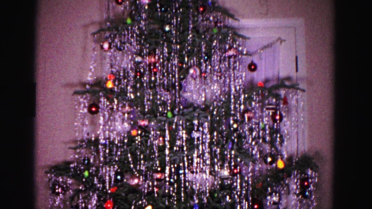 Christmas tree with cascading silver tinsel and colorful glass ornaments, static camera framing similar to preceding frame.