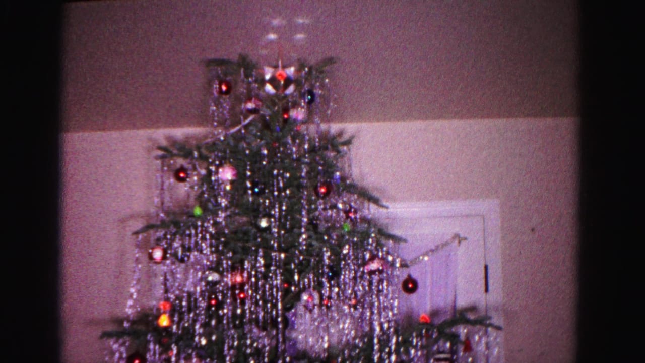 8mm home movie frame, c.1962, Hagerstown Maryland: natural Christmas tree hung with cascading silver tinsel and red and green ornaments, star topper visible, white interior door in background.