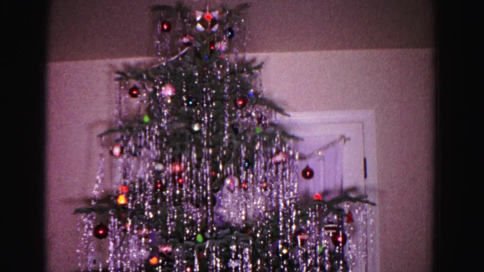 8mm home movie frame, c.1962, Hagerstown Maryland: Christmas tree with layered silver icicle tinsel and multicolored ornaments centered in frame, white paneled door behind lower branches.