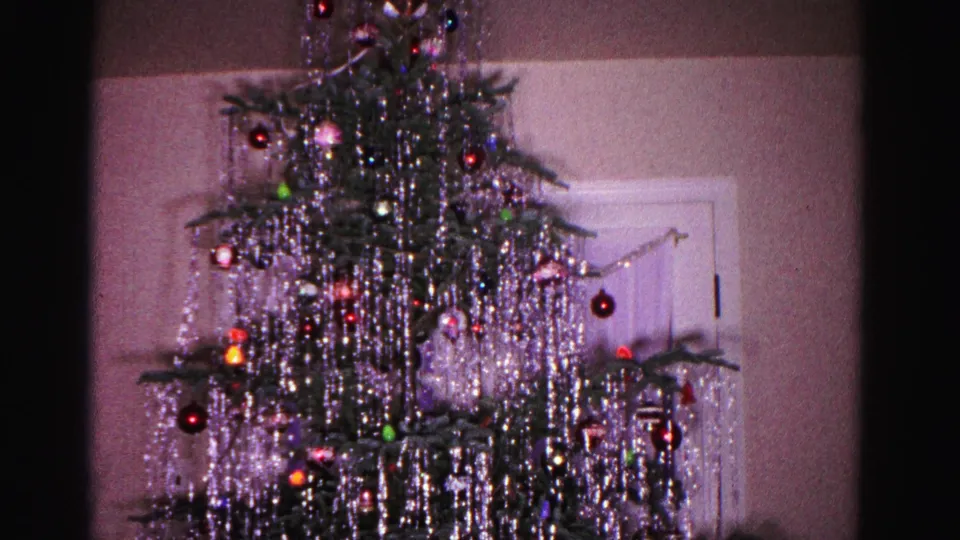 8mm home movie frame, c.1962, Hagerstown Maryland: Christmas tree laden with draping silver tinsel and multicolored glass ball ornaments, star topper at apex, white door visible in background.