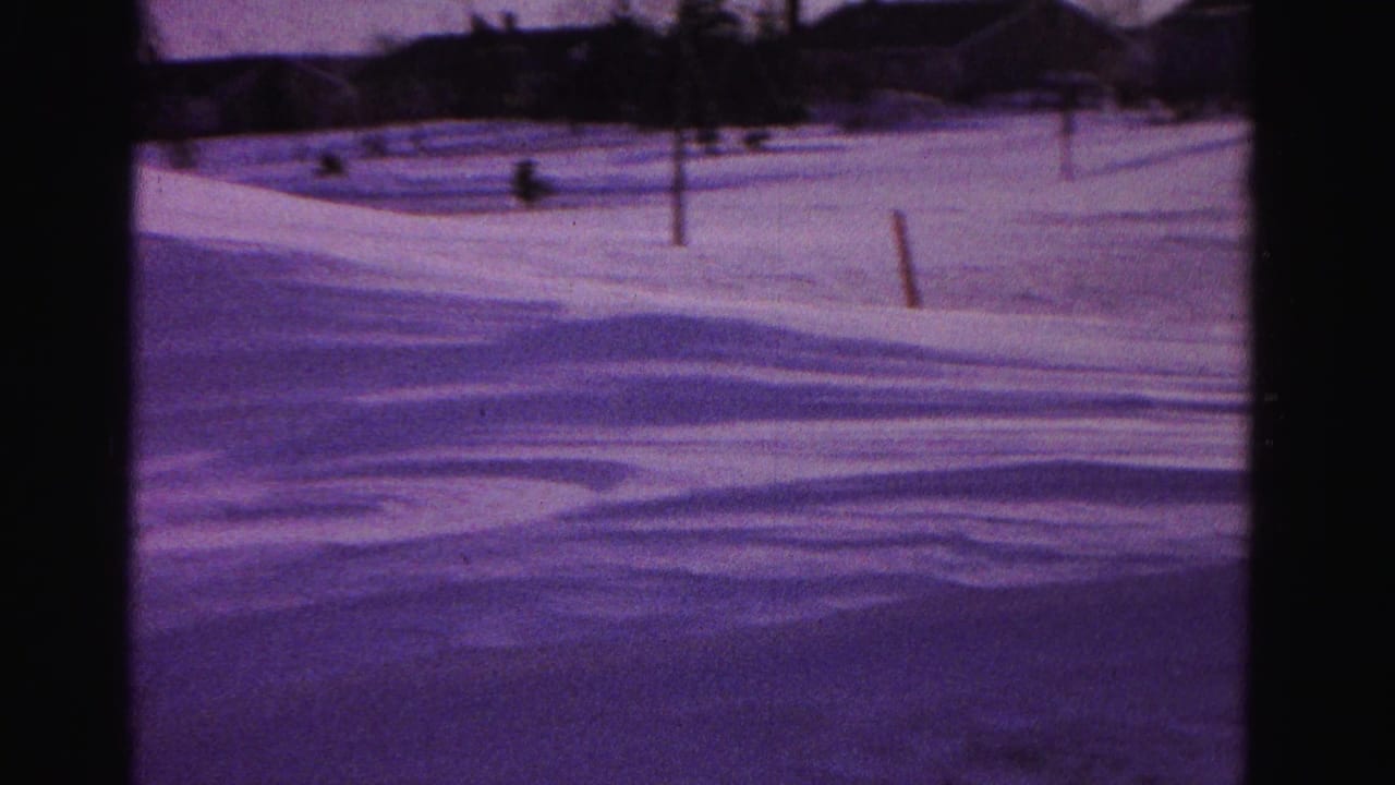 Purple-tinted 8mm frame of deep snow drifts in a residential yard, circa 1962, Hagerstown, Maryland, with utility pole and distant houses visible