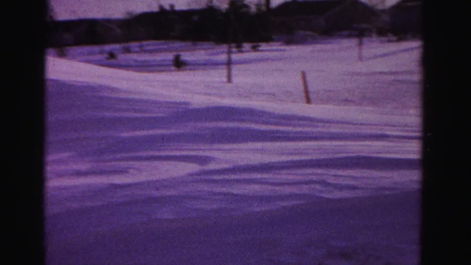 Purple-tinted 8mm frame of deep snow drifts in a residential yard, circa 1962, Hagerstown, Maryland, with utility pole and distant houses visible
