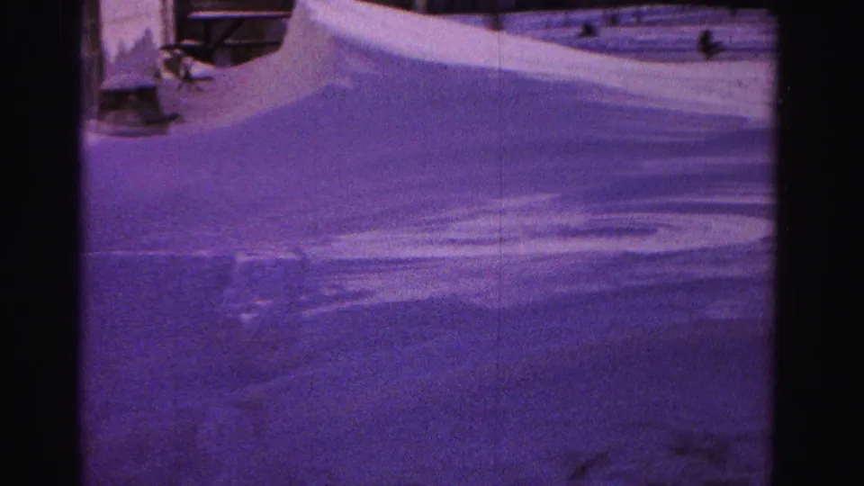 Purple-tinted 8mm frame showing heavy snow accumulation and partial view of a structure or outbuilding at right edge, circa 1962