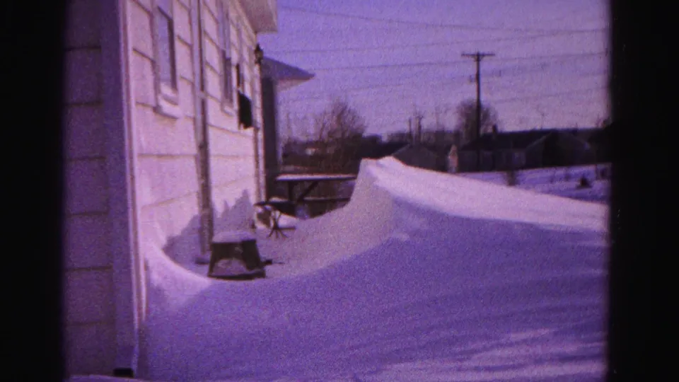 8mm frame of white clapboard house siding, deep snowdrifts, wooden utility pole with overhead lines, and bare deciduous trees; Hagerstown, Maryland, circa 1962