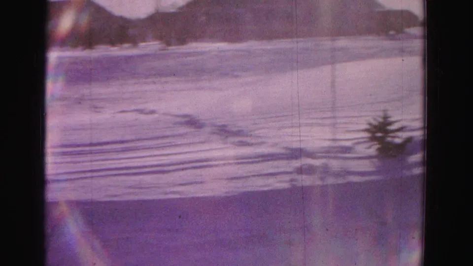 Camera pans to open snow-covered yard; small conical evergreen and distant rooftops visible; lens-flare artifact at lower left; Hagerstown, Maryland area, circa 1962, 8mm home movie.