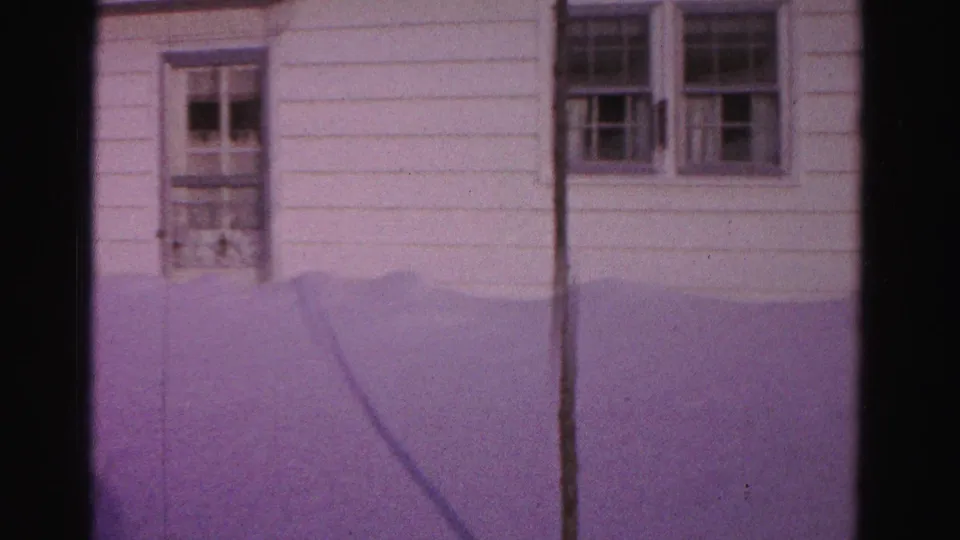 8mm home movie, c.1962, Hagerstown, Maryland — white-sided house showing door with glass panes, double-hung windows, wall-mounted box, and diagonal utility wire against snow-covered ground; purple dye-shift cast.