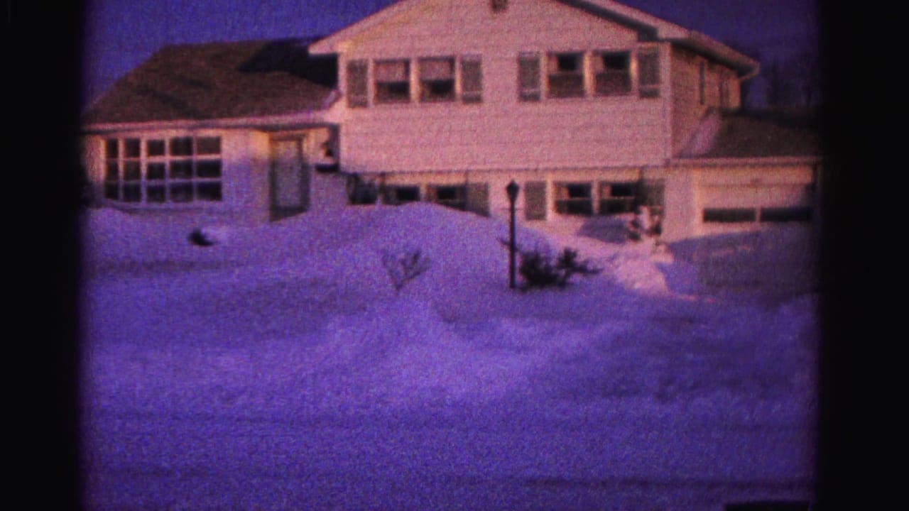 White two-story suburban house with deep snow banks and utility pole at right, 8mm color footage.