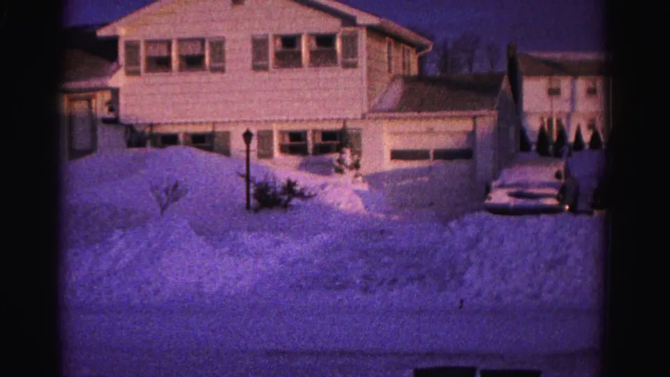 1962 8mm home movie frame showing a suburban house, street lamppost, and deeply buried front yard in a Hagerstown, Maryland, winter scene.