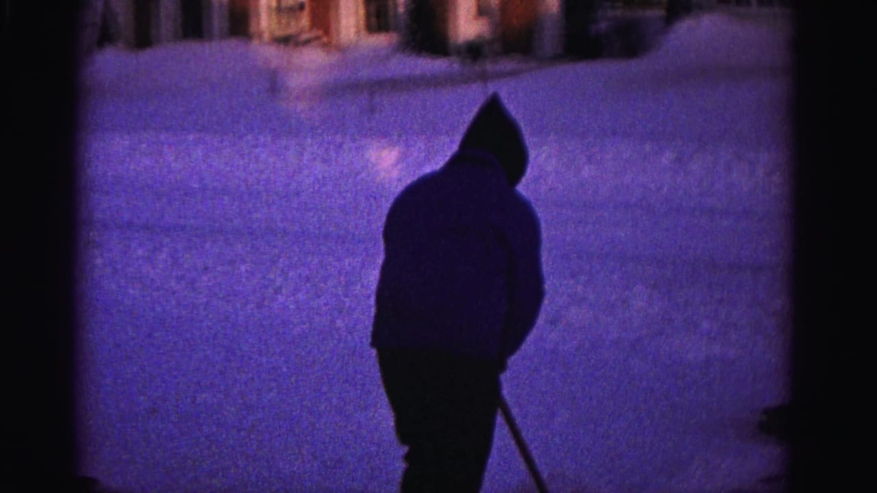 Silhouetted hooded man with snow shovel on residential driveway, deep purple color cast, 8mm home movie, Hagerstown Maryland area, circa 1962.
