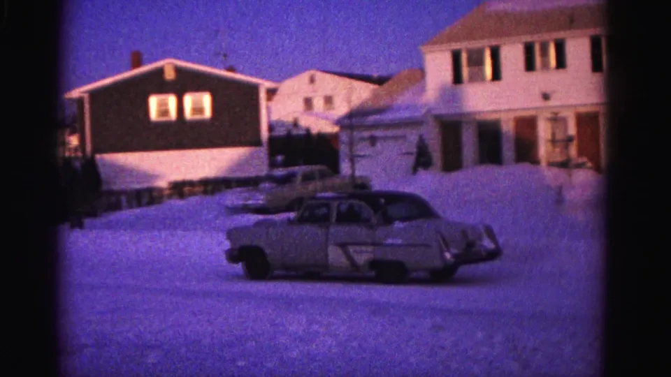 Early 1960s 8mm home movie — suburban winter street; tan sedan, mixed residential houses, small dark figure possibly near car, Hagerstown MD area, 1962.