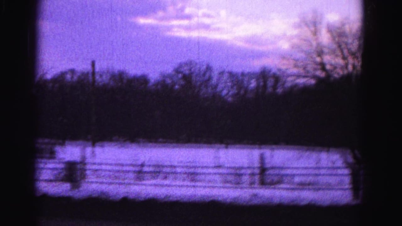 8mm home-movie frame circa 1962 showing a snow-covered field, wire fence, and bare trees under a purple-tinted twilight sky; described as Hagerstown, Maryland area.