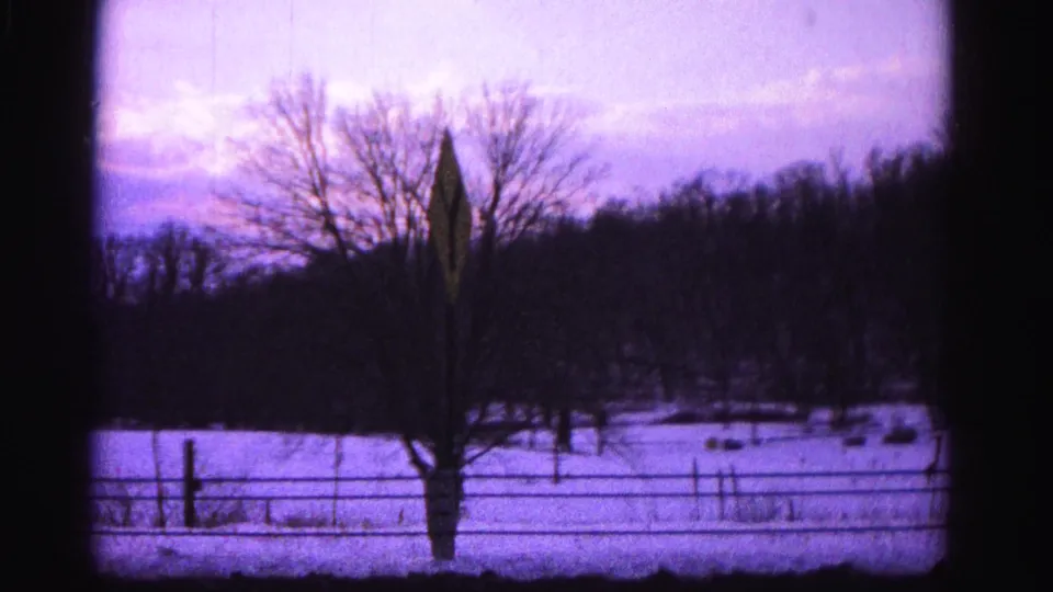 Final frame of 8mm clip circa 1962 showing a settled composition of snowy field, wire fence, bare tree, and diamond road sign; described as Hagerstown, Maryland area per metadata.