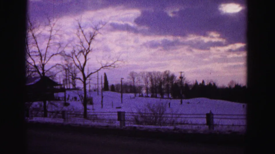 8mm footage, circa 1962 Hagerstown Maryland — snow recreation slope with scattered distant figures, bare trees, wooden fence, and strong purple color cast.