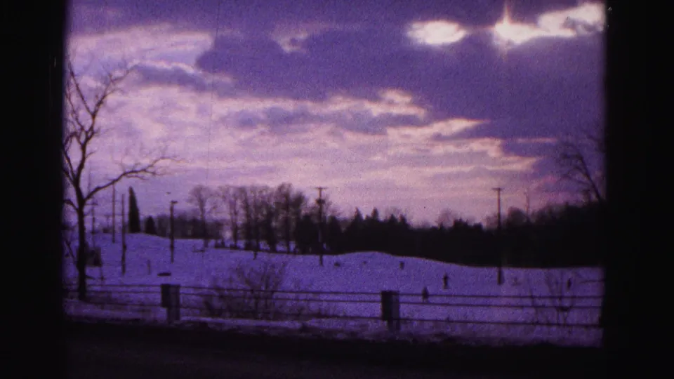 Final frame of 1962 Hagerstown Maryland 8mm footage — wide winter landscape with snow slope, wooden fence, utility poles, bare trees, and characteristically aged purple color cast.