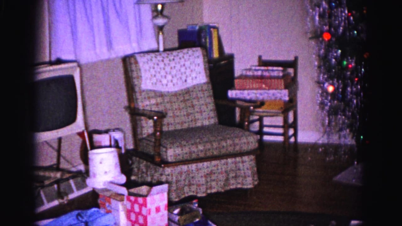 Living room with an upholstered chair, small television, side table, wrapped gifts, and part of a Christmas tree.