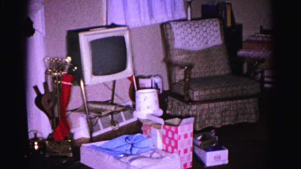 1962 Hagerstown, Maryland home-movie frame showing wrapped presents, a small television, a patterned chair, and holiday objects arranged in a private living room.