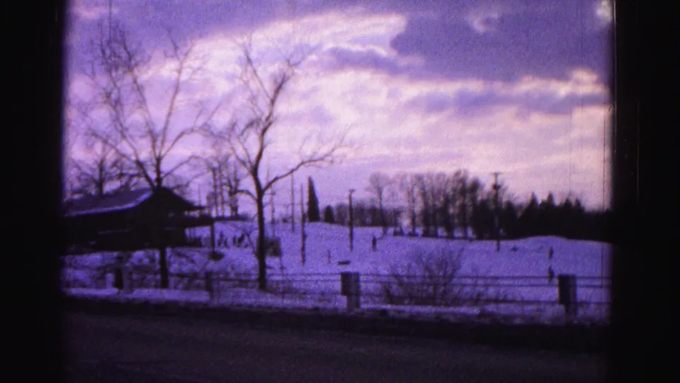 1962 Hagerstown, Maryland winter frame showing a snowy outdoor view with bare trees, fence posts, a road edge, and a clouded sky.