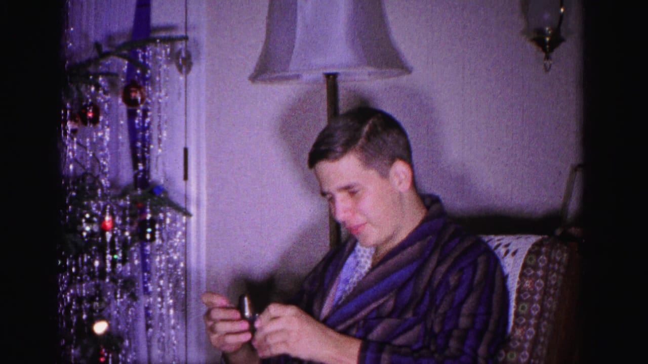 Young man in dark striped bathrobe examines a small Christmas gift, silver tinsel tree with colored ornaments in background, 8mm home movie, Hagerstown Maryland, 1962.