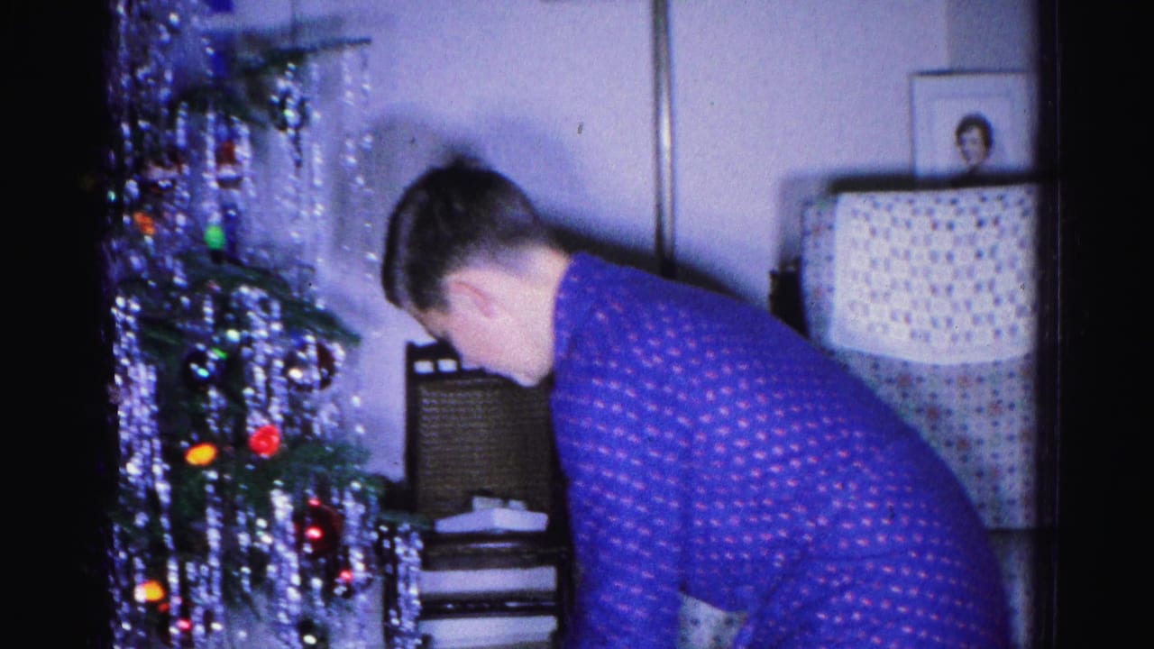 Young man in blue polka-dot pajamas pausing near a decorated Christmas tree in a mid-century living room, Hagerstown, Maryland, circa 1962.
