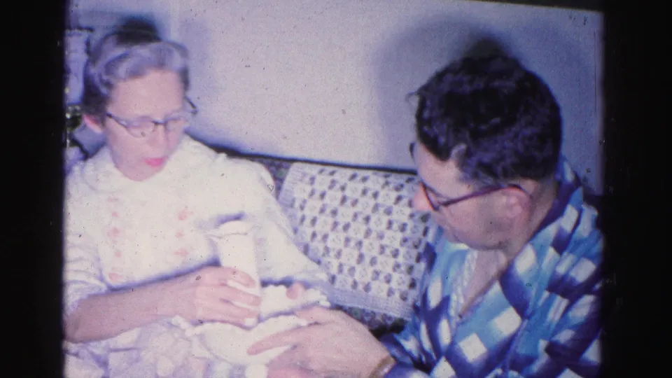 Elderly woman in light patterned top holding a swaddled infant while an elderly man in blue plaid leans in beside her, Hagerstown, Maryland, circa 1962.