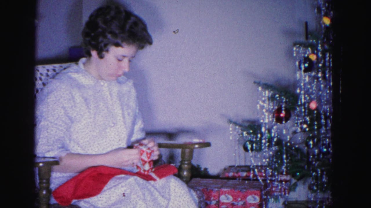 Woman in white top crocheting red yarn beside a pedestal side table; tinsel-laden Christmas tree with colorful ornaments visible at right.